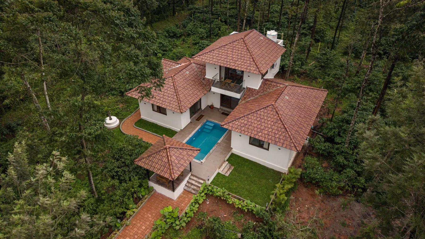 Aerial view of the villa's tiled roofs and blue pool set in thick green forest