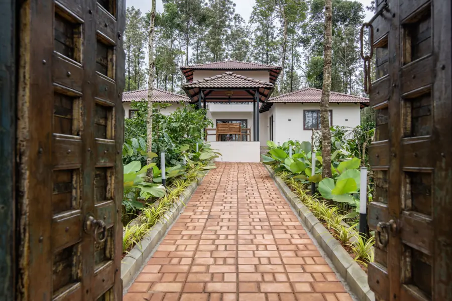 The carved wooden entrance doors open onto a brick path leading to the villa