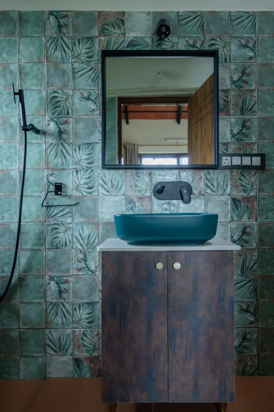 Bathroom with green leaf-patterned tiles and a teal basin