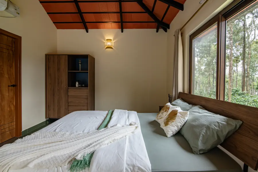 Bed made up with cushions beside corner windows