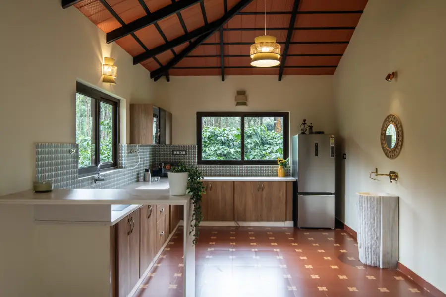 Fitted kitchen with wooden cabinets, a fridge and a window onto the trees