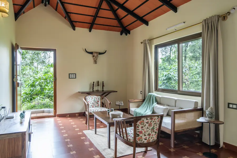 Living room with cane armchairs, a sofa and large windows looking onto coffee plants
