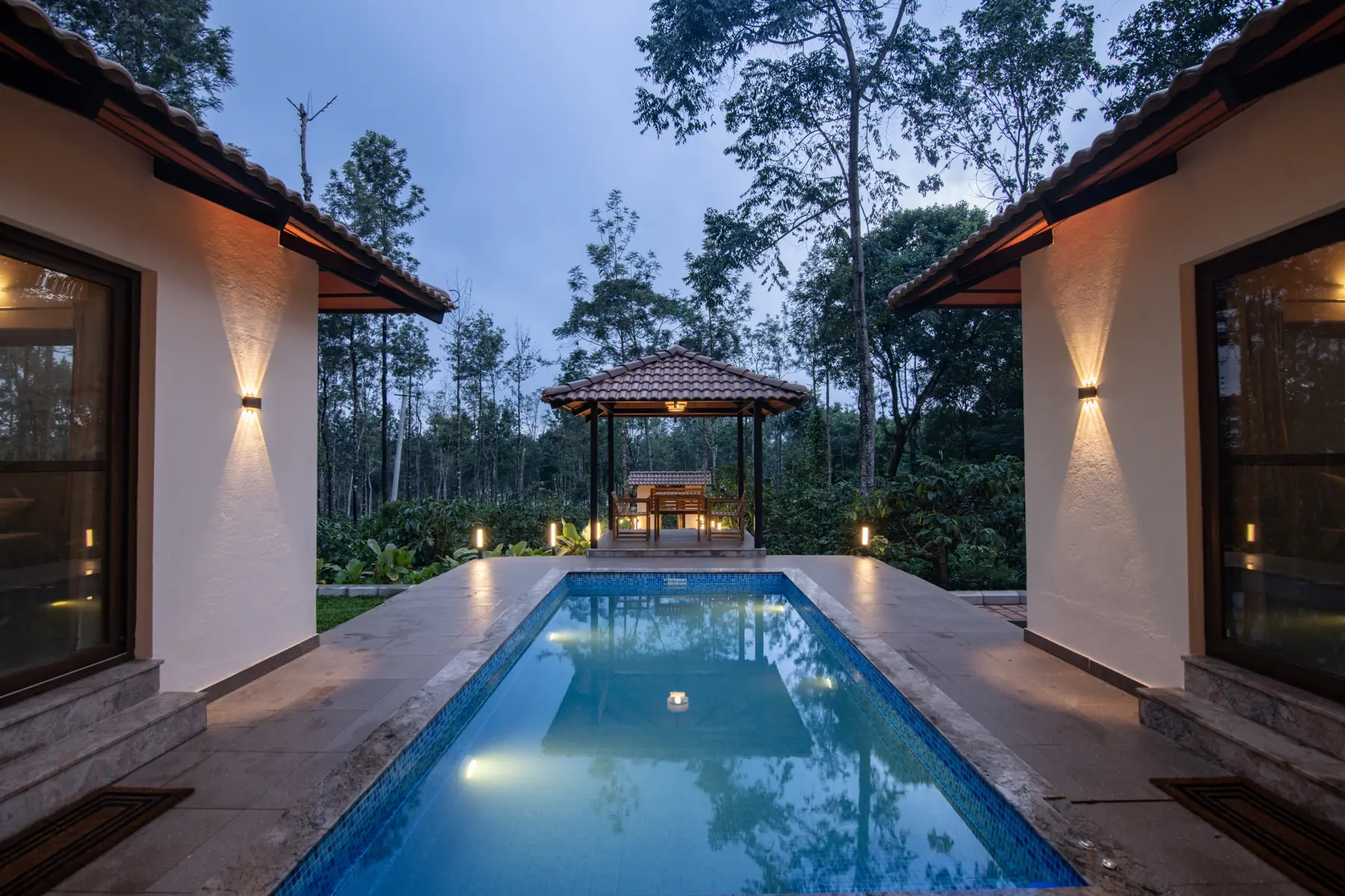The private pool at dusk, lit from within, with the gazebo and trees beyond